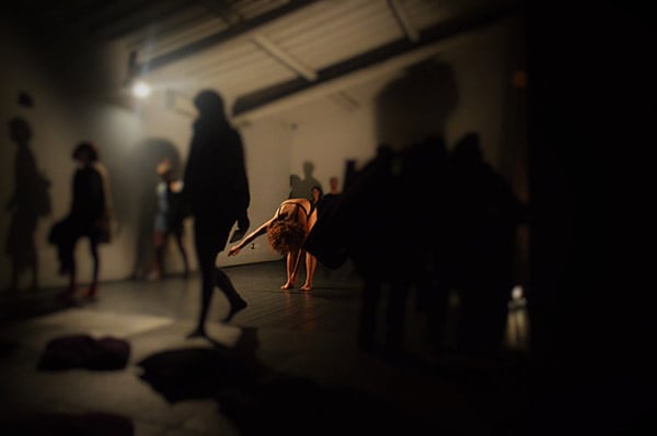 Photo of several performers on stage, only one lit person, the others out of focus in foreground