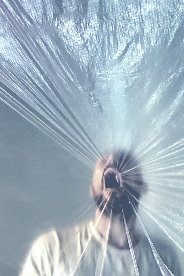 Close-up of a man breathing in a curtain of transparent film with his mouth wide open.