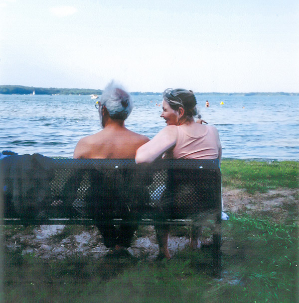 Photo of two elderly people sitting on a bench and looking at the sea